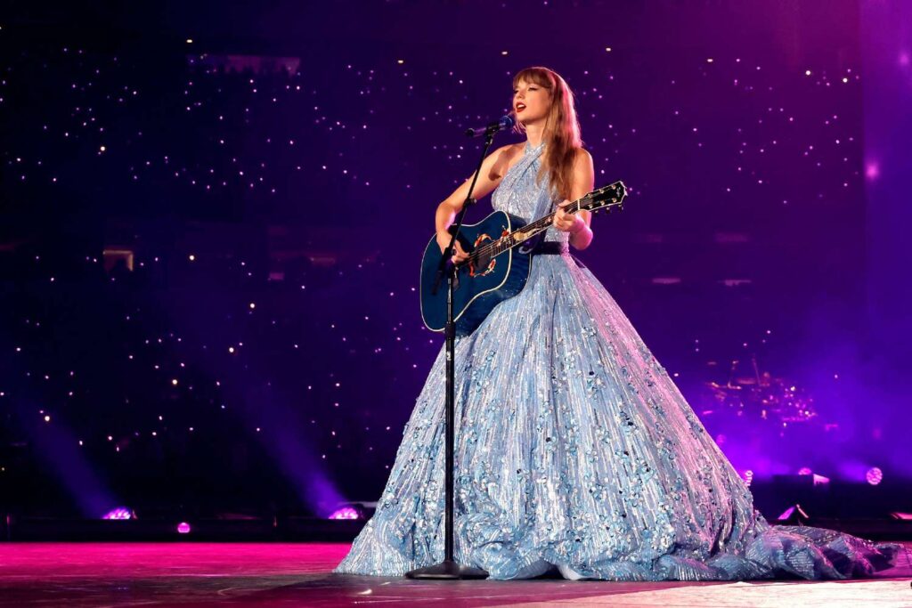 Taylor Swift performing on stage in a gown dress with a guitar during the Eras Tour