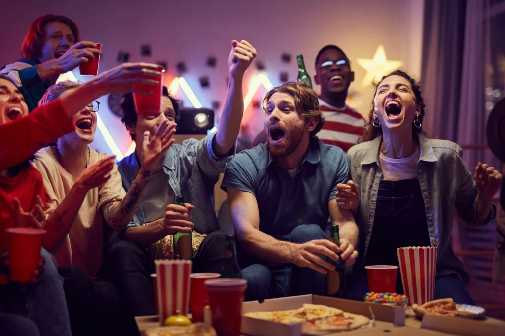 Image of a group of fans cheering at a watch party while watching a game.